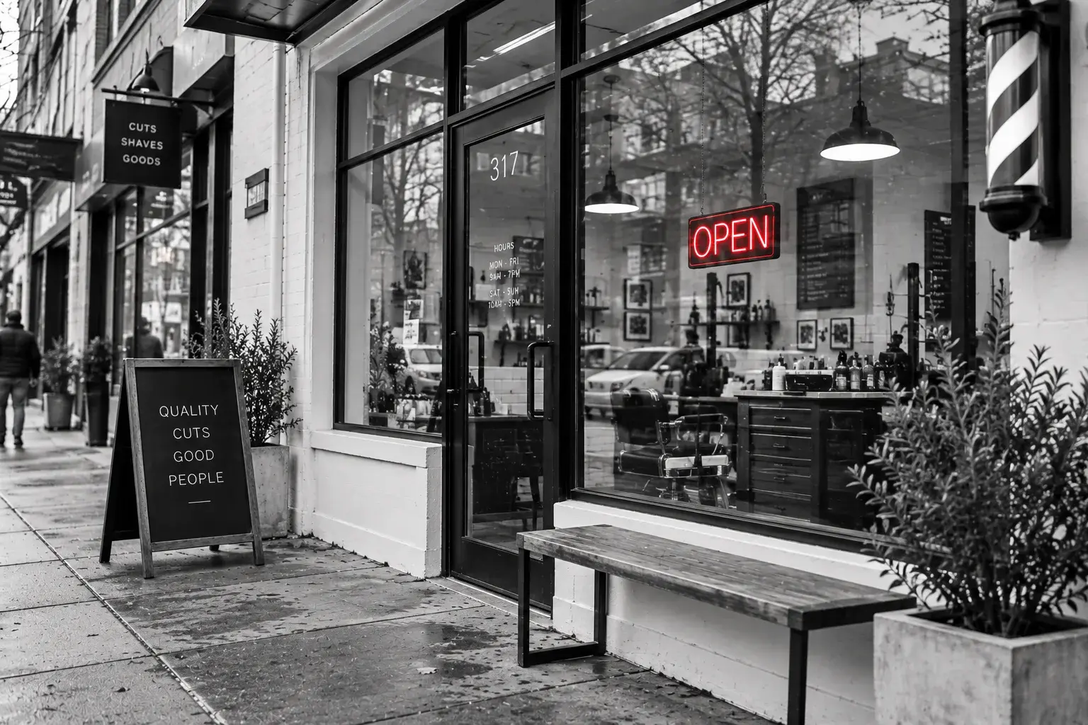 A barbershop storefront with a lit open sign, barber pole and sidewalk sign